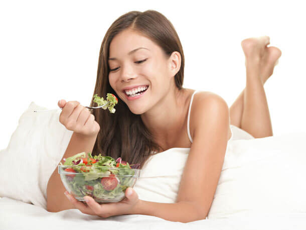 Stock Photo Featuring a Happy Woman Eating a Salad While Laying Down