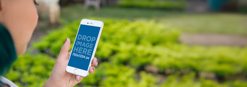 Mockup of a Woman at a Greenhouse Holding a White iPhone