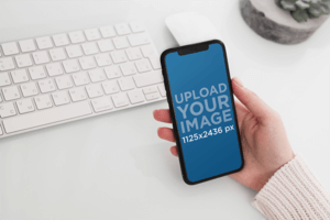 Mockup Featuring A Woman S Hand Holding An Iphone 11 Pro Over A Neat Desk