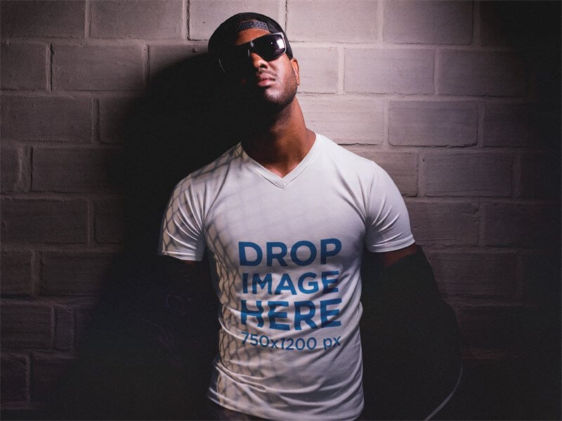 V-Neck T-Shirt Mockup of a Black Man Against a Wall Wearing Sunglasses
