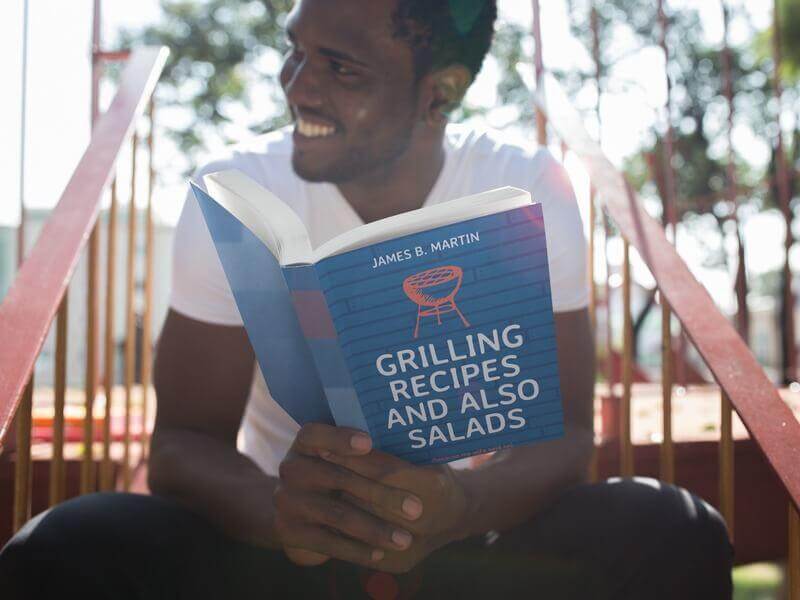 Book Cover Mockup for a Grilling Recipe Book Being Held by a Man