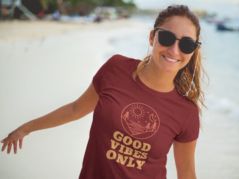 Smiling Lovely Woman Wearing a T-Shirt Mockup and Sunglasses at the Beach