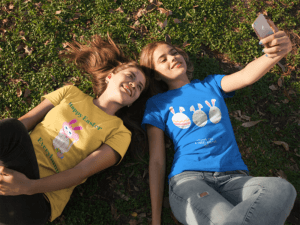 Two Girlfriends Wearing Tees Mockup While Lying On The Grass Taking A Selfie A16280