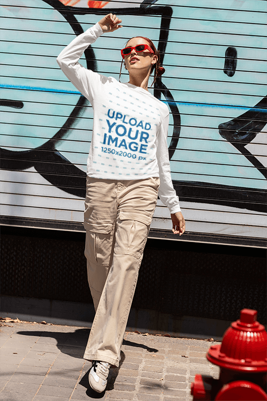 Comfort Colors Long Sleeve Tee Mockup Featuring A Woman Posing Against A Graffiti Wall In The Street