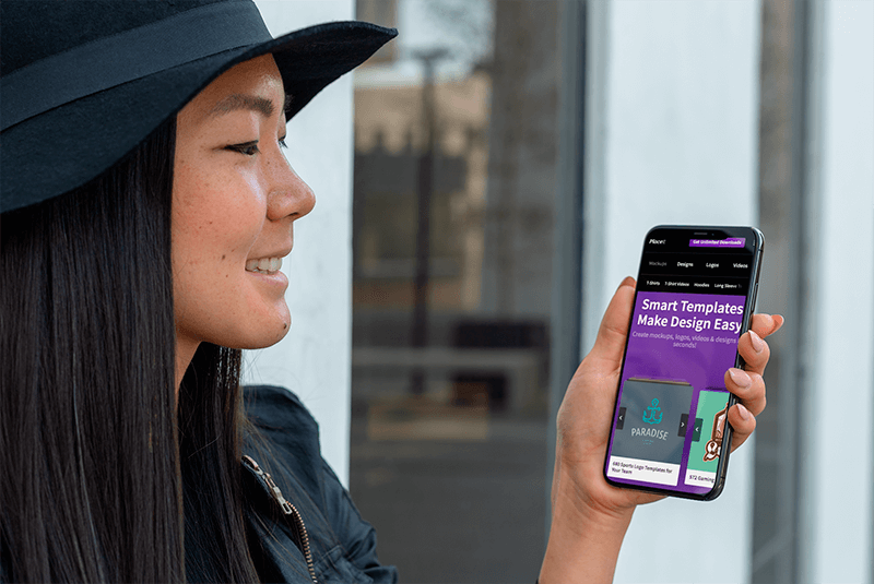 Mockup Of A Smiling Girl With A Hat Holding Her Iphone Xs Max In An Urban Scenario