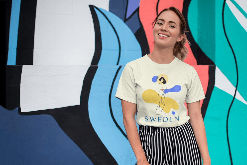 Tee Mockup Of A Smiling Girl In Front Of A Wall With Colorful Illustrations