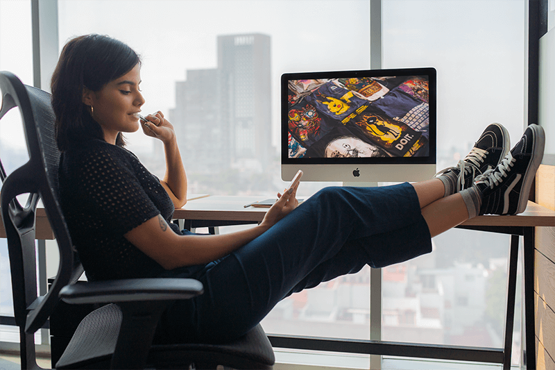 Girl Checking Her Phone At The Office Near An Imac Mockup