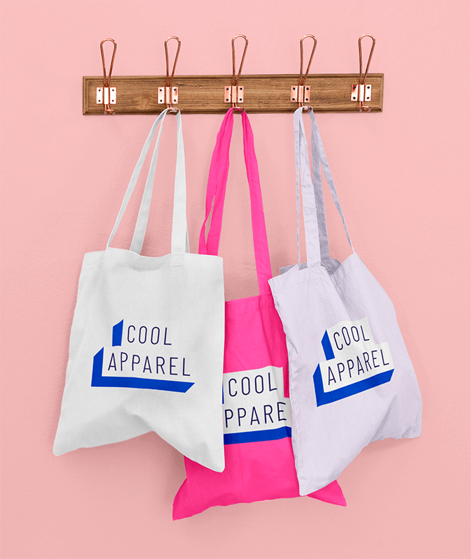 Mockup Of Three Customizable Tote Bags Hanging Against A Solid Color Wall