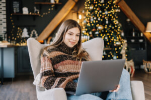 Young Caucasian Woman Using Laptop Computer In Holidays At Home In The Armchair In Living Room.