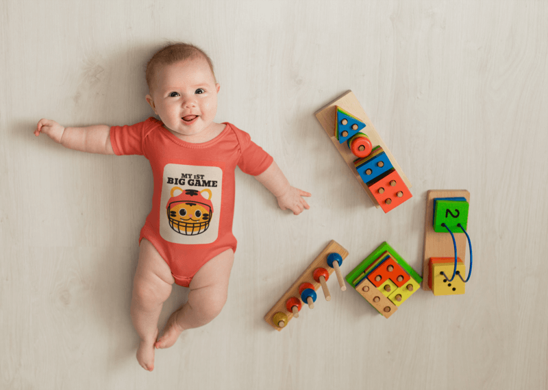 Mockup Of A Baby Wearing A Onesie Featuring Some Toys