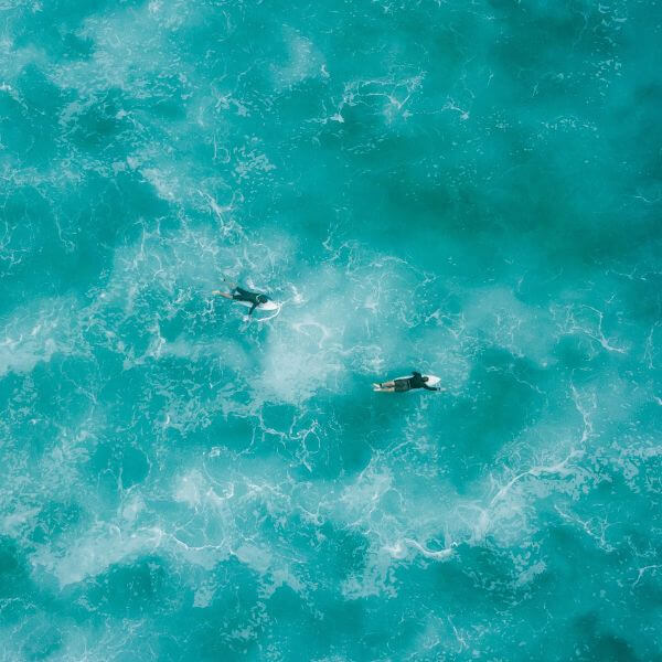 A Beautiful Turquoise Photo Of The Ocean With Two Surfers On It