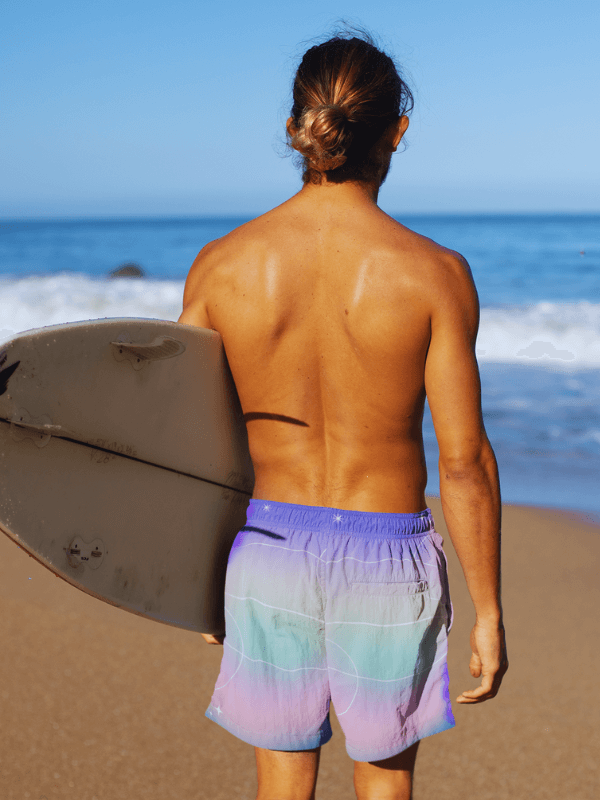 A Young Man Wearing Custom Shorts On A Beach Day While Holding His Surfing Board