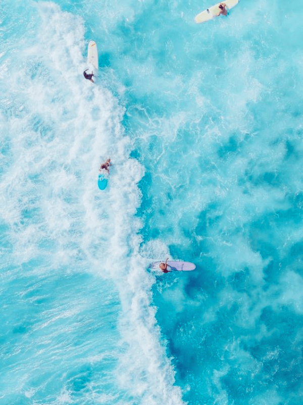 An Aerial View Of The Turquoise Ocean With Surfers Enjoying The Freshness Of Summer