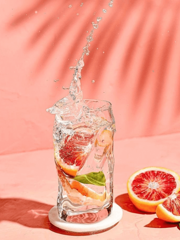 An Aesthetic And Refreshing Pink Grapefruit Beverage Served In A Glass, With Some Pink Fruits On The Side