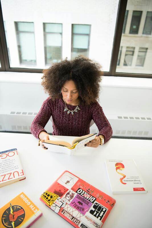 Photo Of A Woman Sitting On A Desk And Reading By Pexels