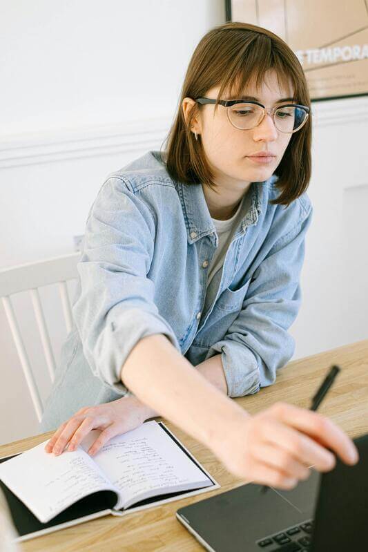 Photo Of A Woman Writing On A List While Looking At The Computer By Pexels