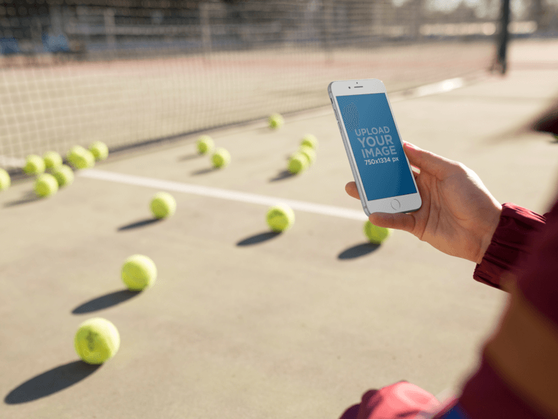 Product Mockup Of A Woman Holding An iPhone In Portrait Position While At A Tennis Court