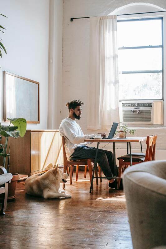 Photo Of A Man Working From Home With His Dog Lying On A Wooden Floor By Pexels