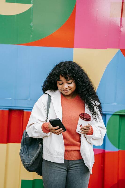 Photo Of A Smiling Woman Using Smartphone Near Colorful Wall By Pexels