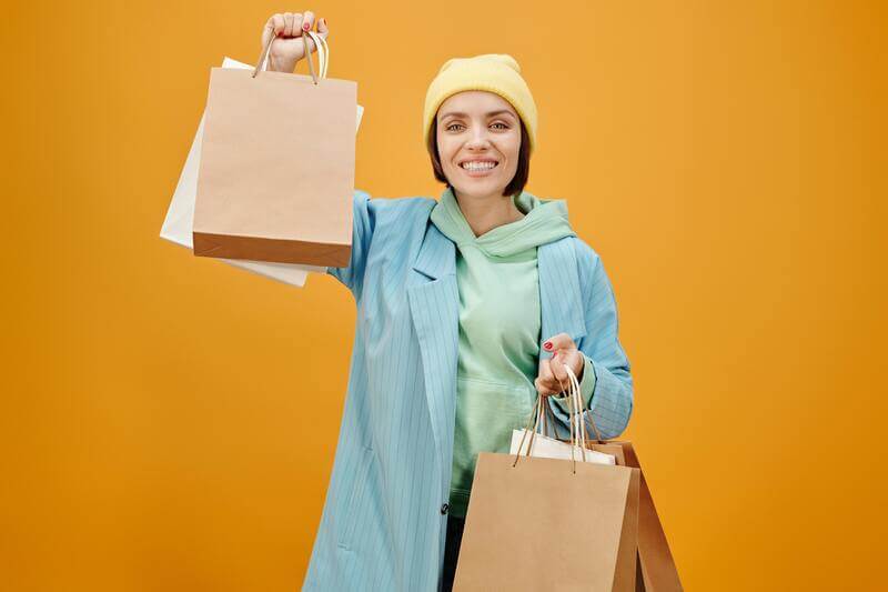 Photo Of A Smiling Woman Holding Shopping Bags On A Plain Background By Pexels