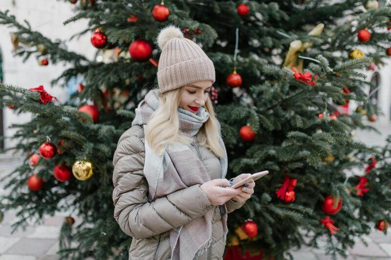 Photo Of A Woman Viewing Her Phone In Front Of A Christmas Tree By Pexels