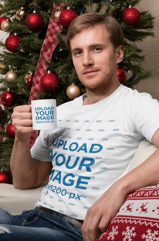 T Shirt Mockup Of A Man Holding An 11 Oz Mug Sitting In Front Of A Christmas Tree