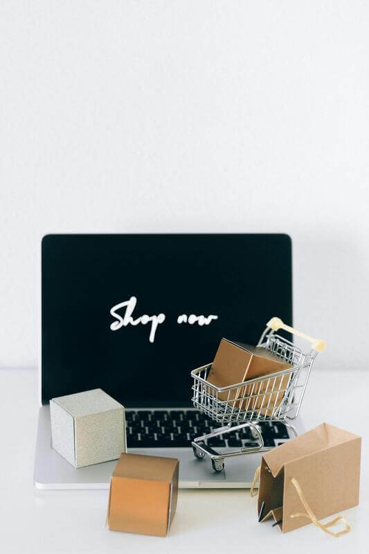 Photo Of A Laptop Alongside Small Boxes And A Shopping Cart By Pexels