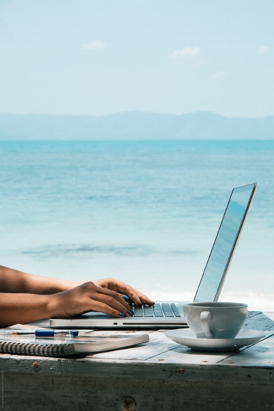 A Laptop With Hands On It, With The Ocean As The Main Background