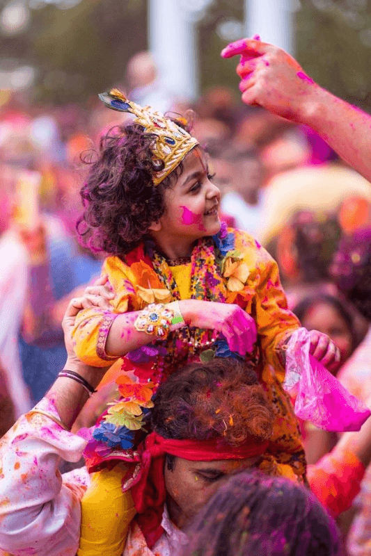 A Beautiful, Smiling Little Girl Wearing A Crown While Sitting On Her Dad's Shoulders, Celebrating The Spirit Of The Holi Festival