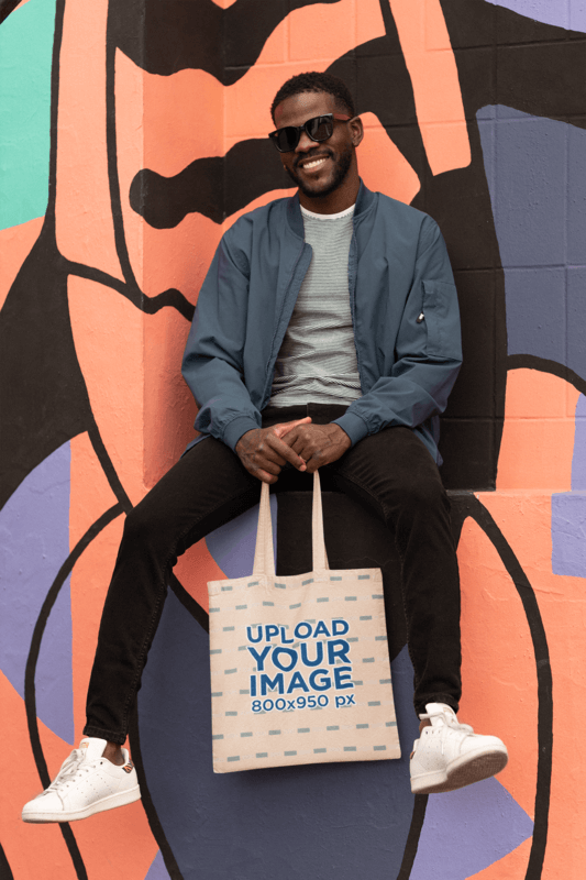 Tote Bag Mockup Featuring A Cheerful Man Posing Behind A Colorful Wall