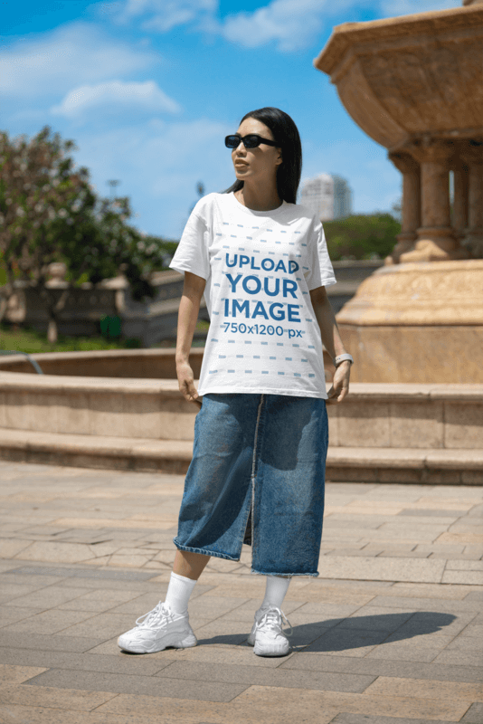 Bella Canvas 3001 T Shirt Mockup Featuring A Woman With Sunglasses Posing Near A Fountain