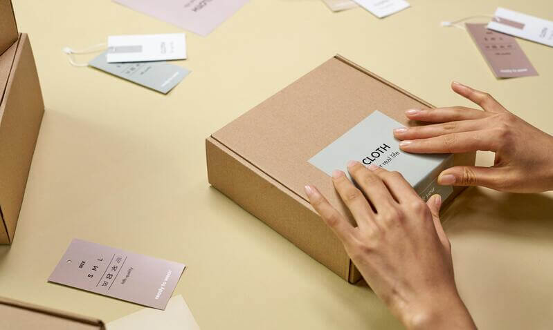Photo Of Apparel Tags Scattered Across A Surface And A Pair Of Hands Adding A Sticker To A Box By Pexels